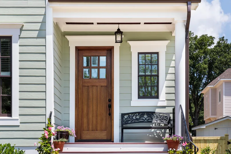 green siding on home with new wood brown door