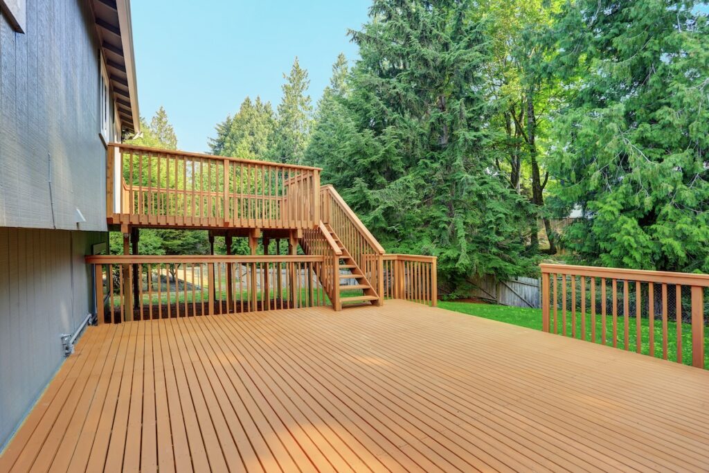 Backyard view of grey rambler house with upper and lower decks