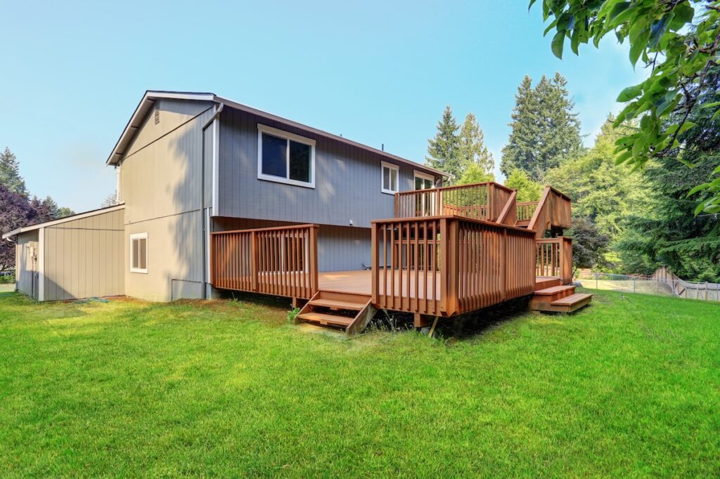 Backyard view of grey rambler house with upper and lower decks
