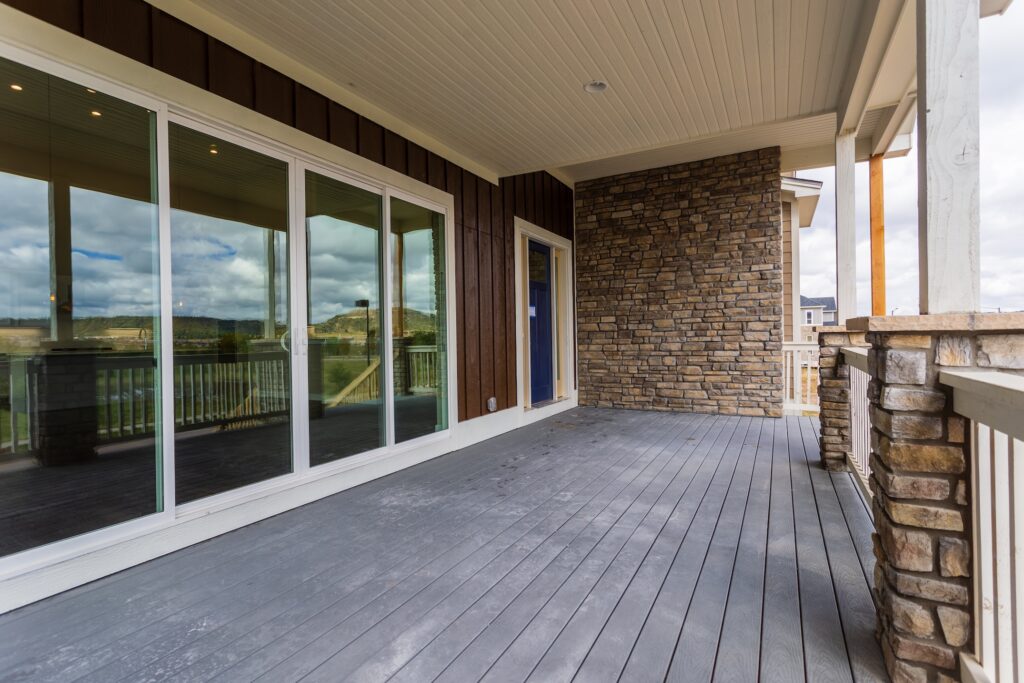 Large front porch with a window-wall, stone, brick, pillars and railing
