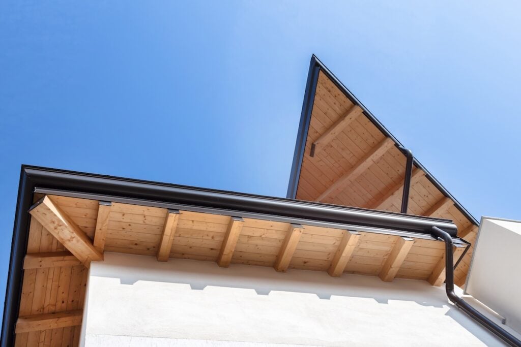New wooden warm ecological house roof with steel gutter rain system. Professional construction and drainage pipes installation. Eco materials.