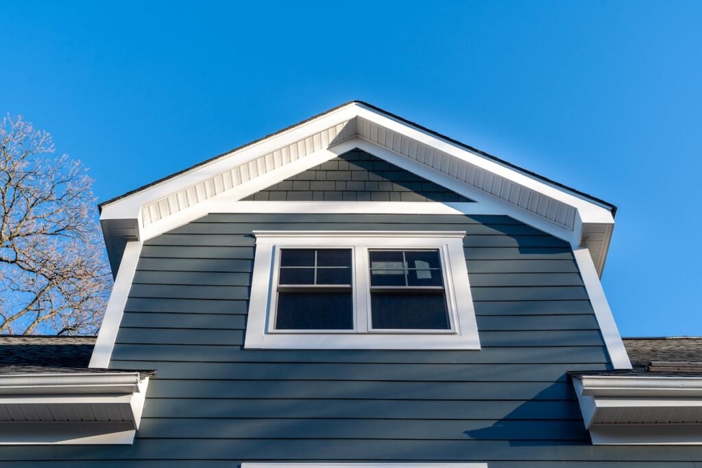 New restoration facade with double hung window w/ fixed top sash and bottom sash that slides up,  divided by two white grilles, thick elegant frame, blue vinyl siding contrasting white corner, gable