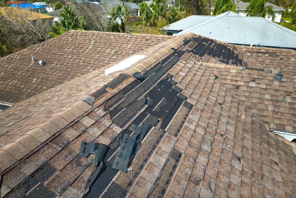Damaged house roof with missing shingles after hurricane Ian in Florida. Consequences of natural disaster. wind damage to roof