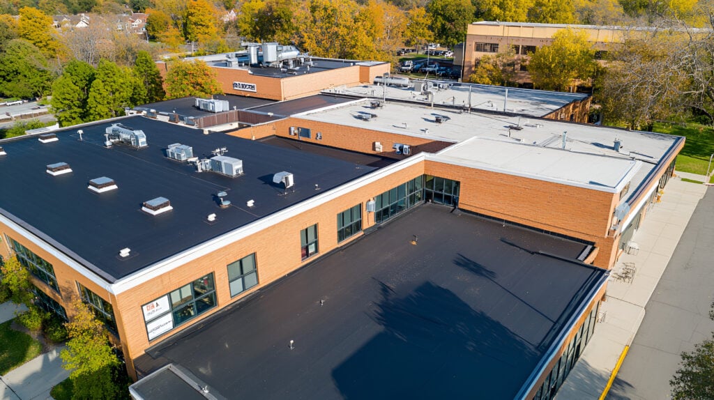 Drone-captured images of commercial buildings with asphalt shingles and TPO membrane roofs on a sunny day