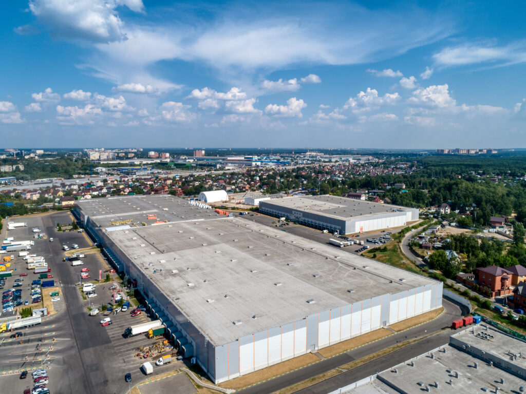 Huge warehouse building with flat roof and cars on parking site under blue sky with fluffy clouds near city in summer bird eye view Albert Lea commercial roofing