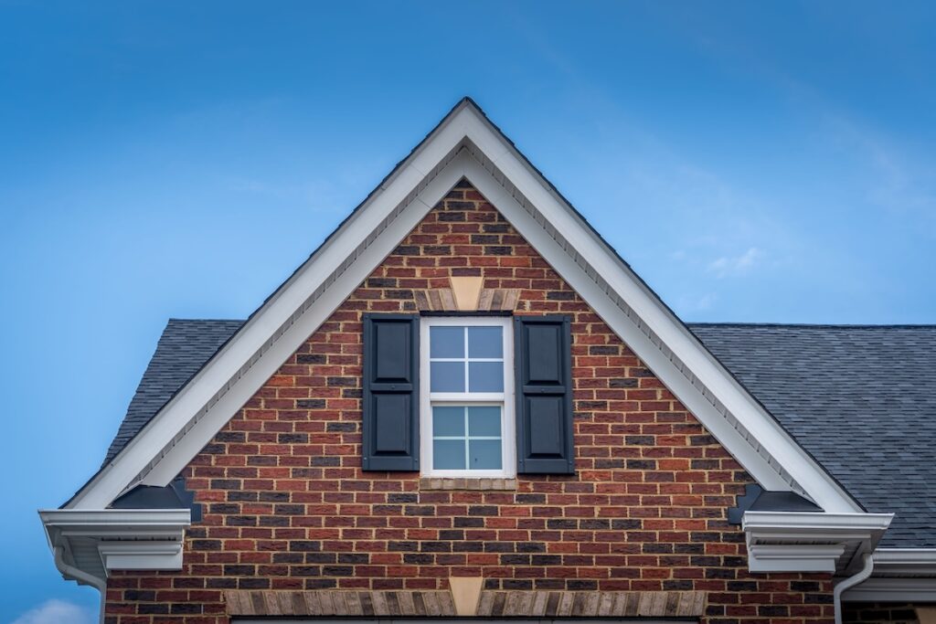 types of siding Gable with red brick facade siding, double hung window with white frame, vinyl shutters on a pitched roof attic at a luxury American single family home neighborhood USA