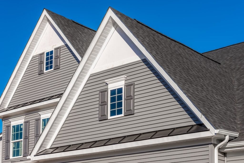 house siding colors Double gable, with white decorative trim over the windows on a triangle gable roof, white soffit and fascia,  gray horizontal vinyl lap siding with blue sky background