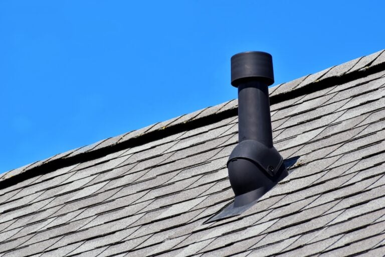 Black air ventilation chimney on grey shingles roof of residental house on blue sky background