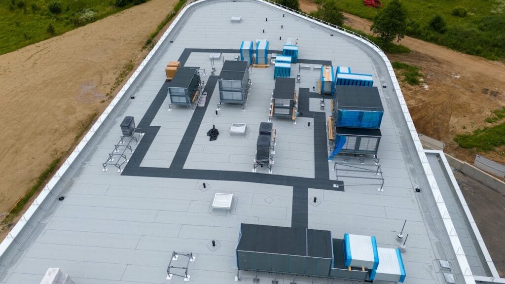 flat roof ventilation Aerial view of a commercial building rooftop featuring various HVAC units, ventilation systems. The flat roof is mostly gray with black pathways.