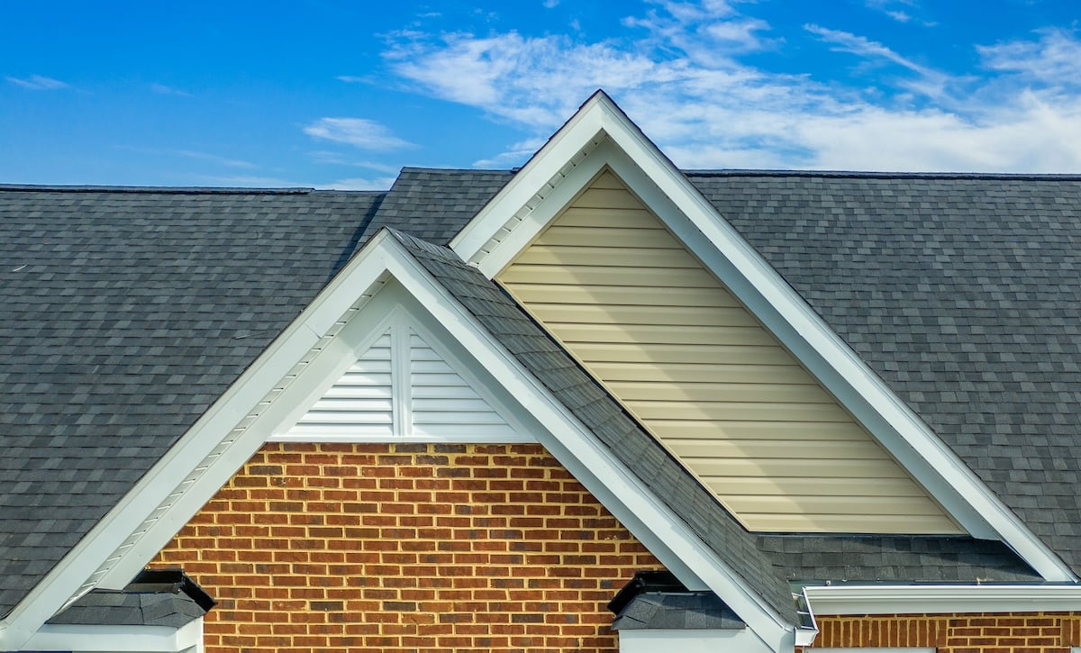 certainteed roof shingles Double gable with beige horizontal vinyl lap and red brick facade siding, with triangle shape white attic vent on a pitched roof attic at an American single family home neighborhood USA