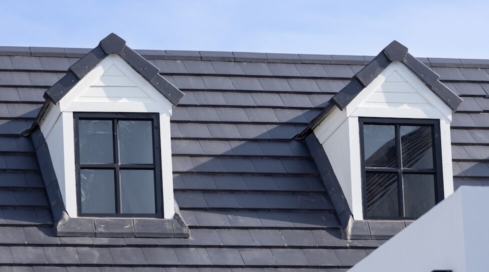 slate roof cost Two windows on a roof with a blue sky in the background. The roof is made of metal and has a slanted design