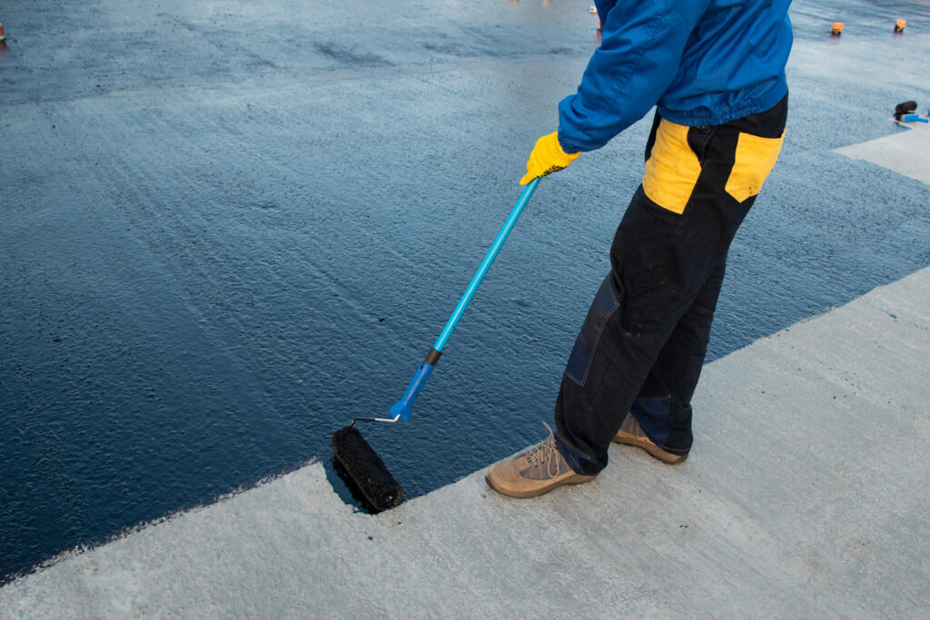 commercial roof coatings Waterproofing coating. Worker applies bitumen mastic on the foundation. Roofer cover the rooftop polymer modified bitumen waterproofing primer, with a roller brush.