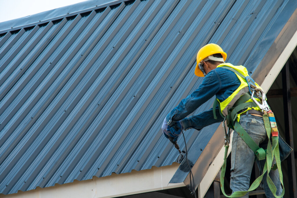 commercial metal roof Construction worker wearing safety harness belt during working on roof structure of building on construction site,Roofer using air or pneumatic nail gun and installing metal roof tile on top new roof.