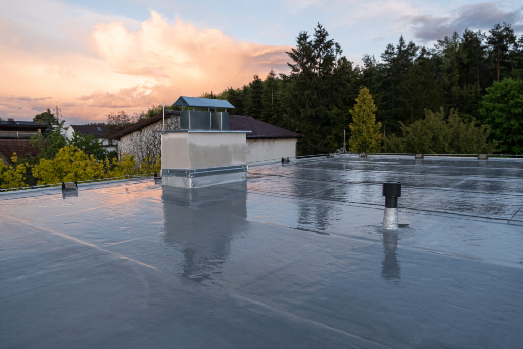 commercial roof coatings Flat roof covered with bitumen membrane and silver lacquer with chimney on a private house. Reflections after rain