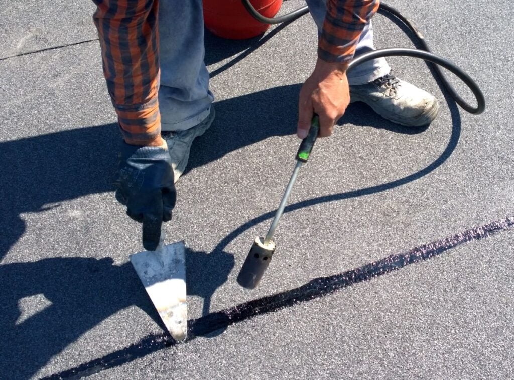 Roofer preparing part of bitumen roofing felt roll for melting by gas heater torch flame