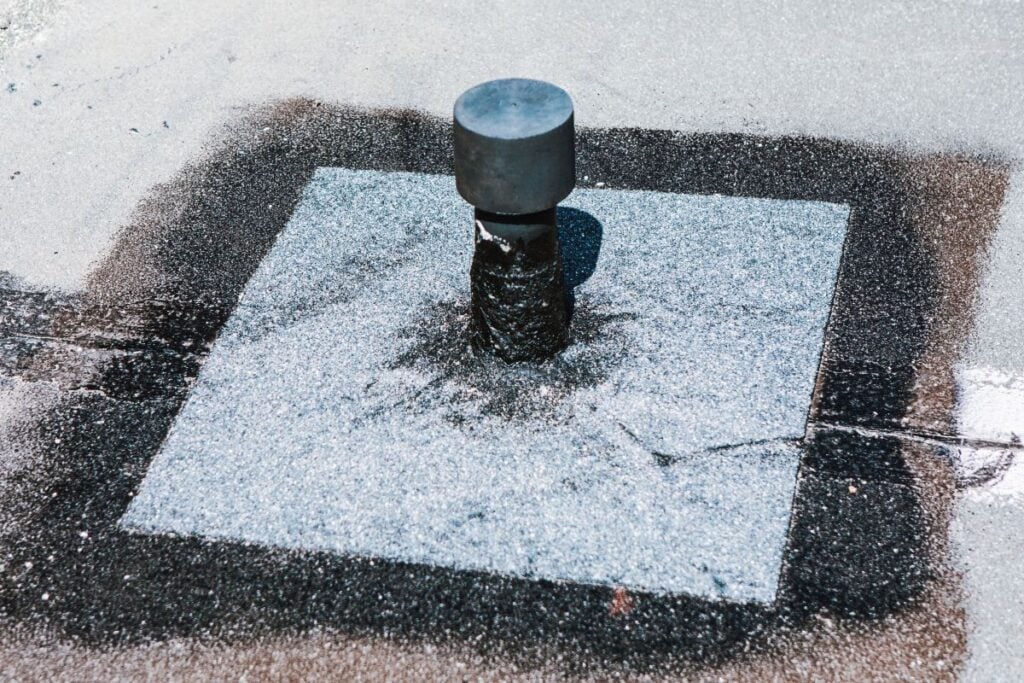 Flat roof vent is installed on a rooftop. Seal looks effective around the base