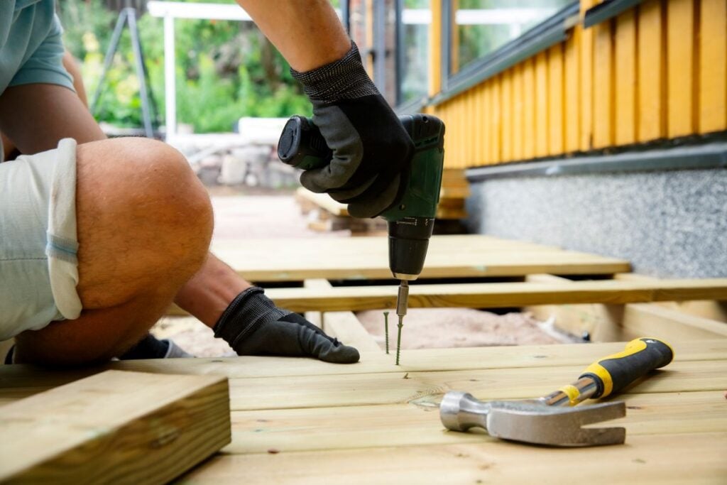 Homeowner using a power drill to install wooden deck planks during a backyard renovation