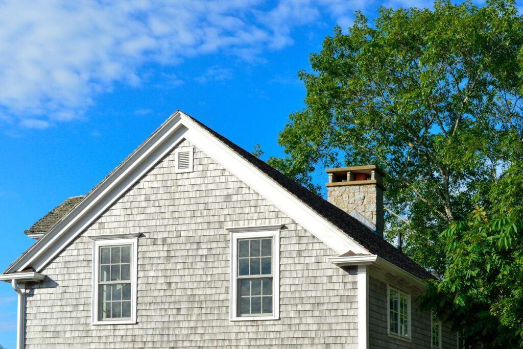 Two storey grey colored vintage building with wood cedar shake siding, two double hung windows
