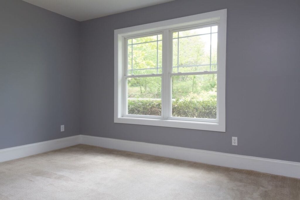 grey room with a big white window facing the woods