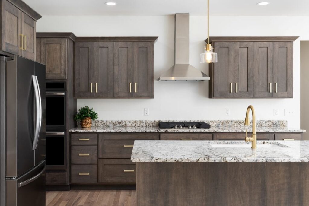 A kitchen detail with a gold faucet on a granite countertop, dark wood cabinets, stainless steel appliances, and gold pendant lights hanging above the island. Kitchen Layout Ideas That Balance Function and Style