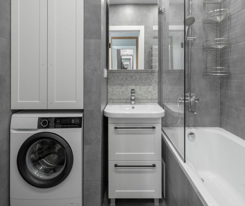 Small modern bathroom in gray tones with washing machine, white vanity, mirrored frame and fittings
