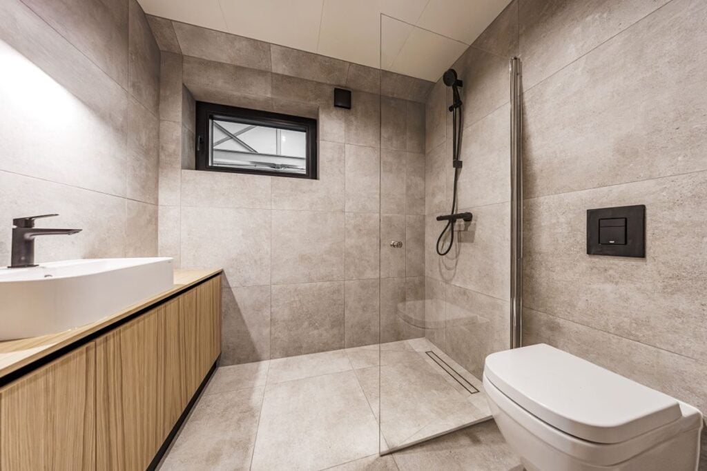 Stylish bathroom interior with light stone tiles, wood vanity, vessel sink, walk-in shower, and matte black fixtures